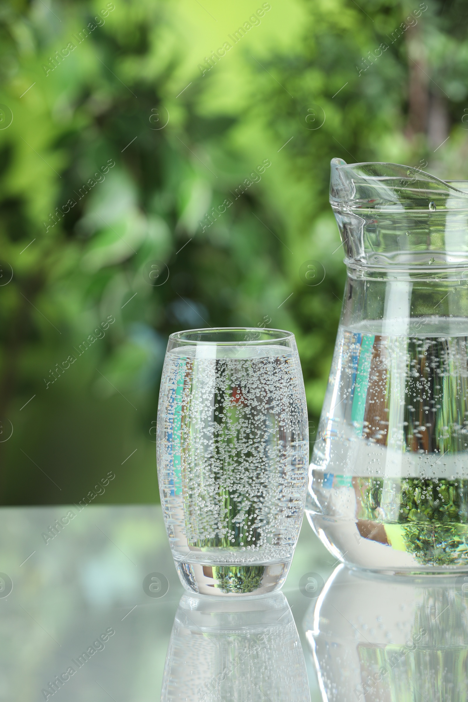 Photo of Soda water in glass and jug on light table outdoors