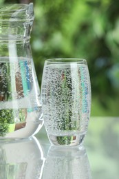 Photo of Soda water in glass and jug on light table outdoors