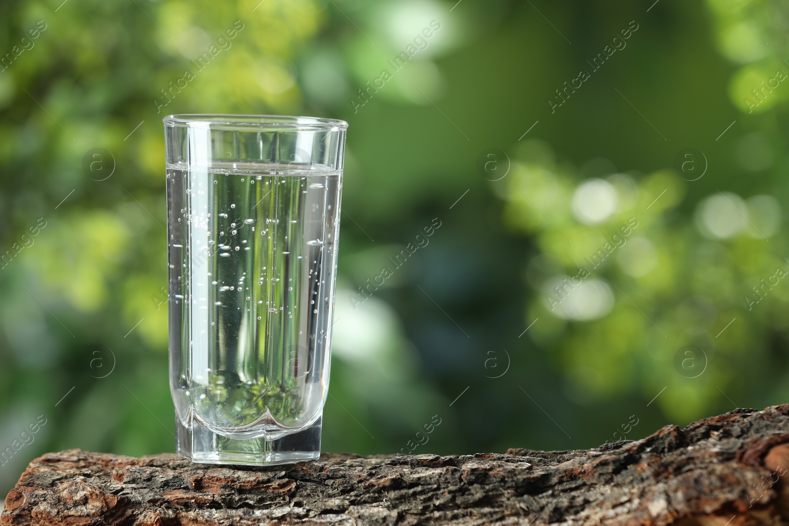 Photo of Soda water in glass on wooden surface outdoors, space for text