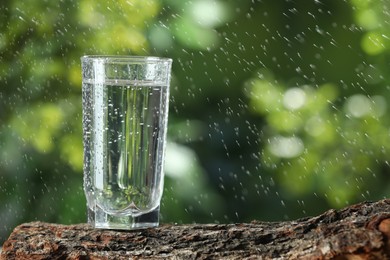 Photo of Soda water in glass on wooden surface under drops outdoors, space for text