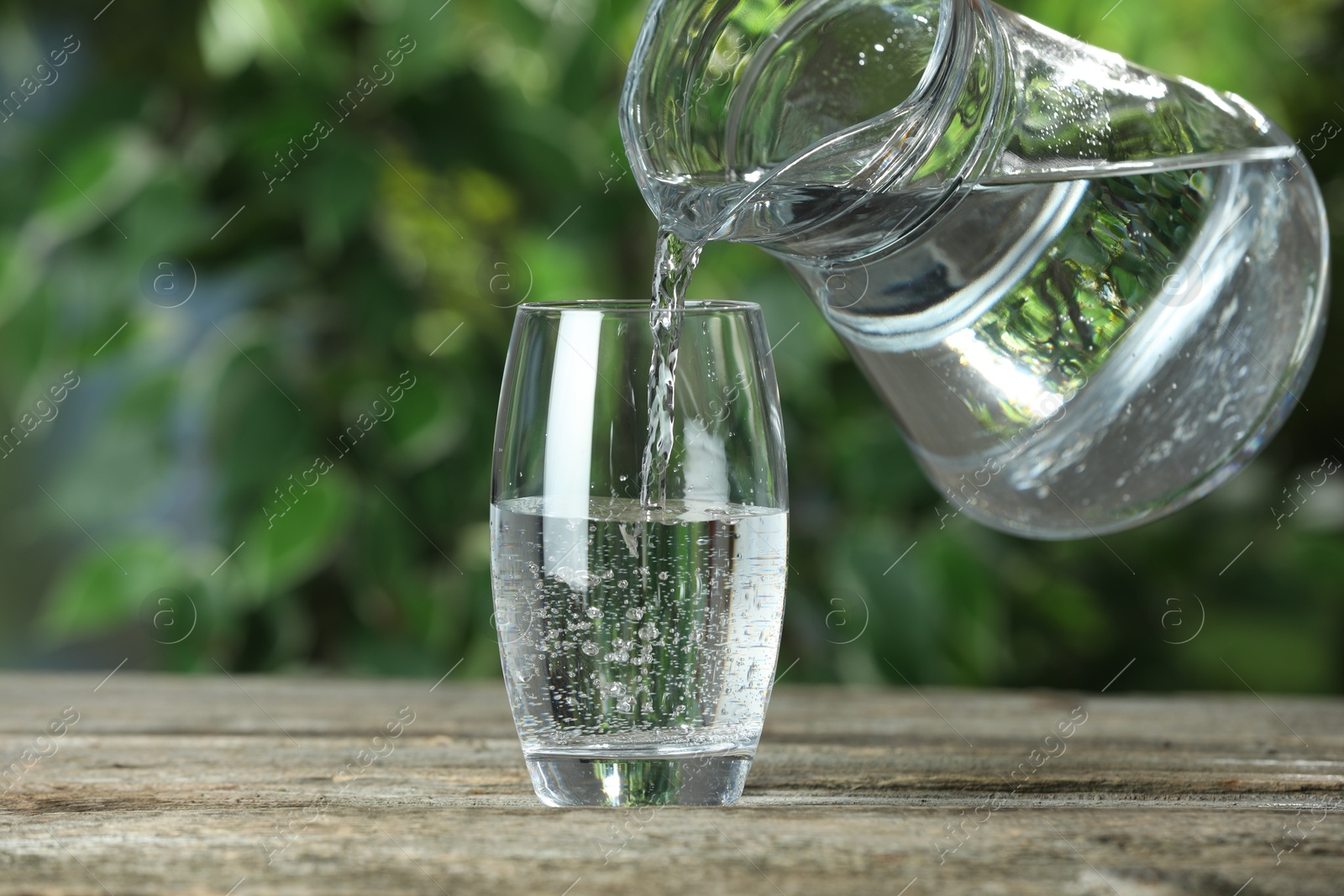 Photo of Pouring soda water in glass at wooden table outdoors