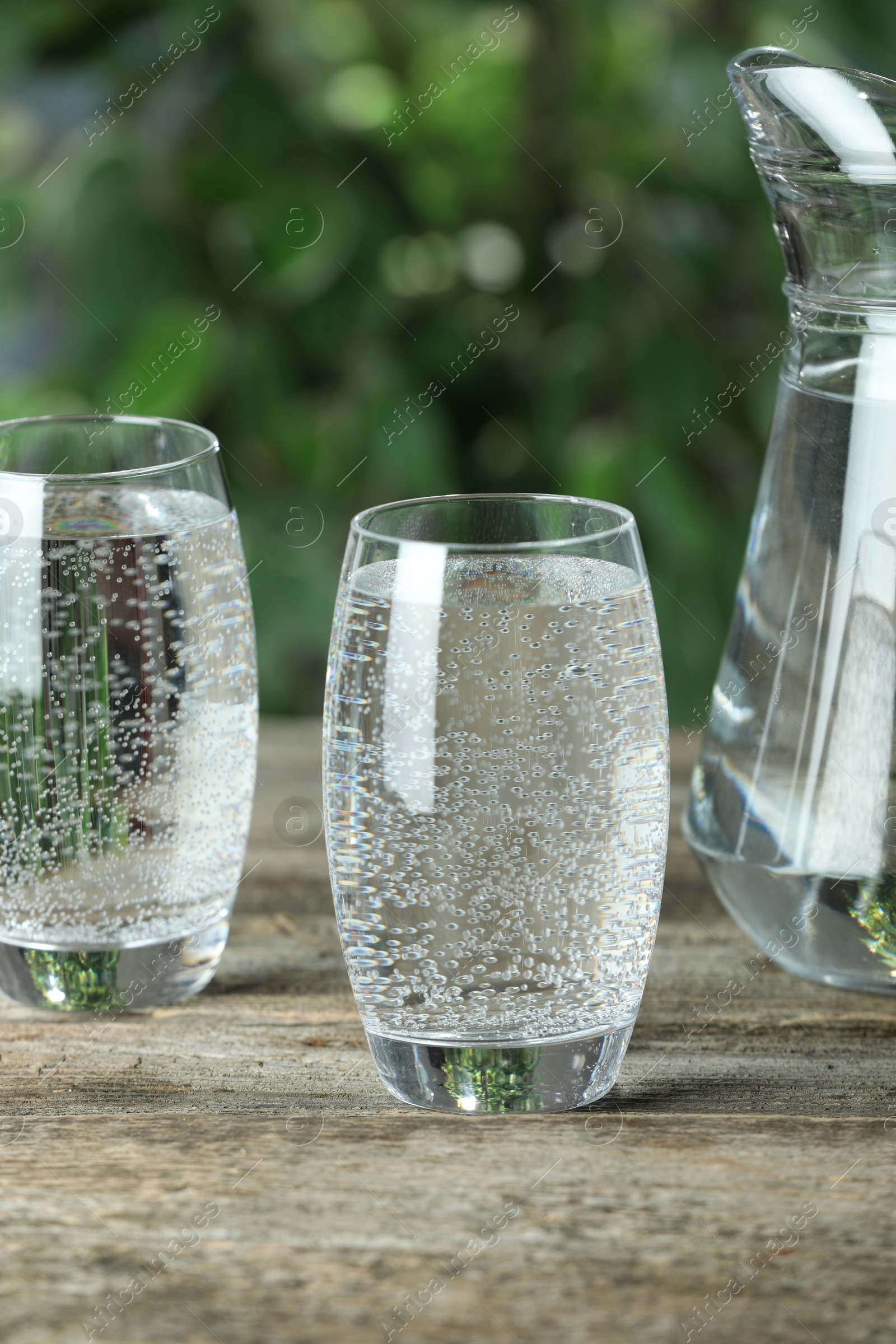 Photo of Soda water in glasses and jug on wooden table outdoors