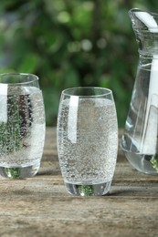 Soda water in glasses and jug on wooden table outdoors