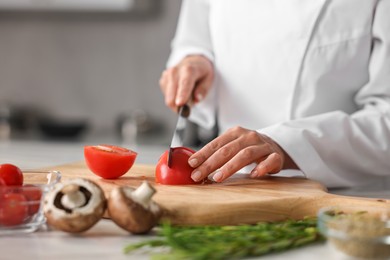 Photo of Professional chef cutting tomato at table in kitchen, closeup