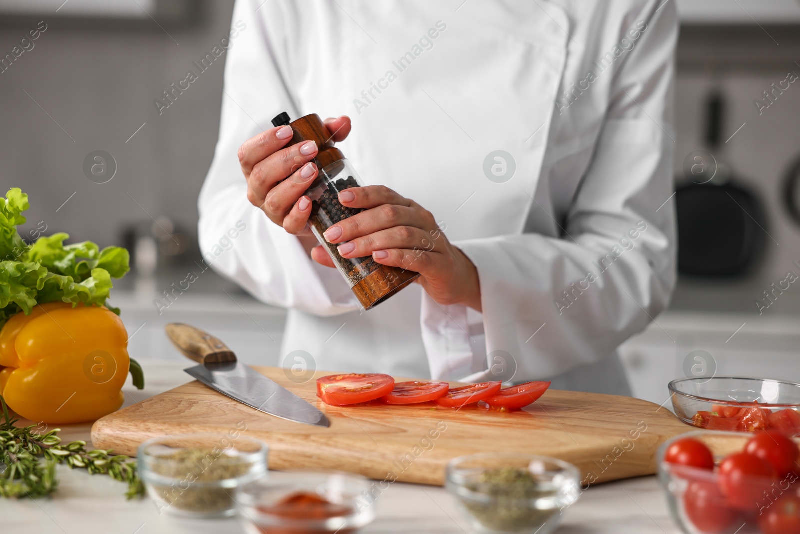 Photo of Professional chef seasoning tomatoes at table in kitchen, closeup