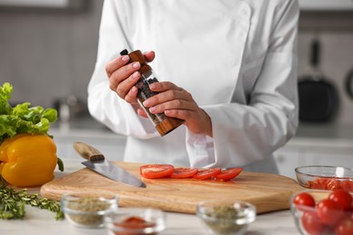 Professional chef seasoning tomatoes at table in kitchen, closeup