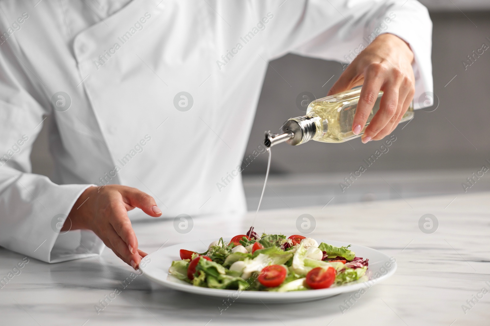 Photo of Professional chef pouring oil onto delicious salad at white marble table in kitchen, closeup