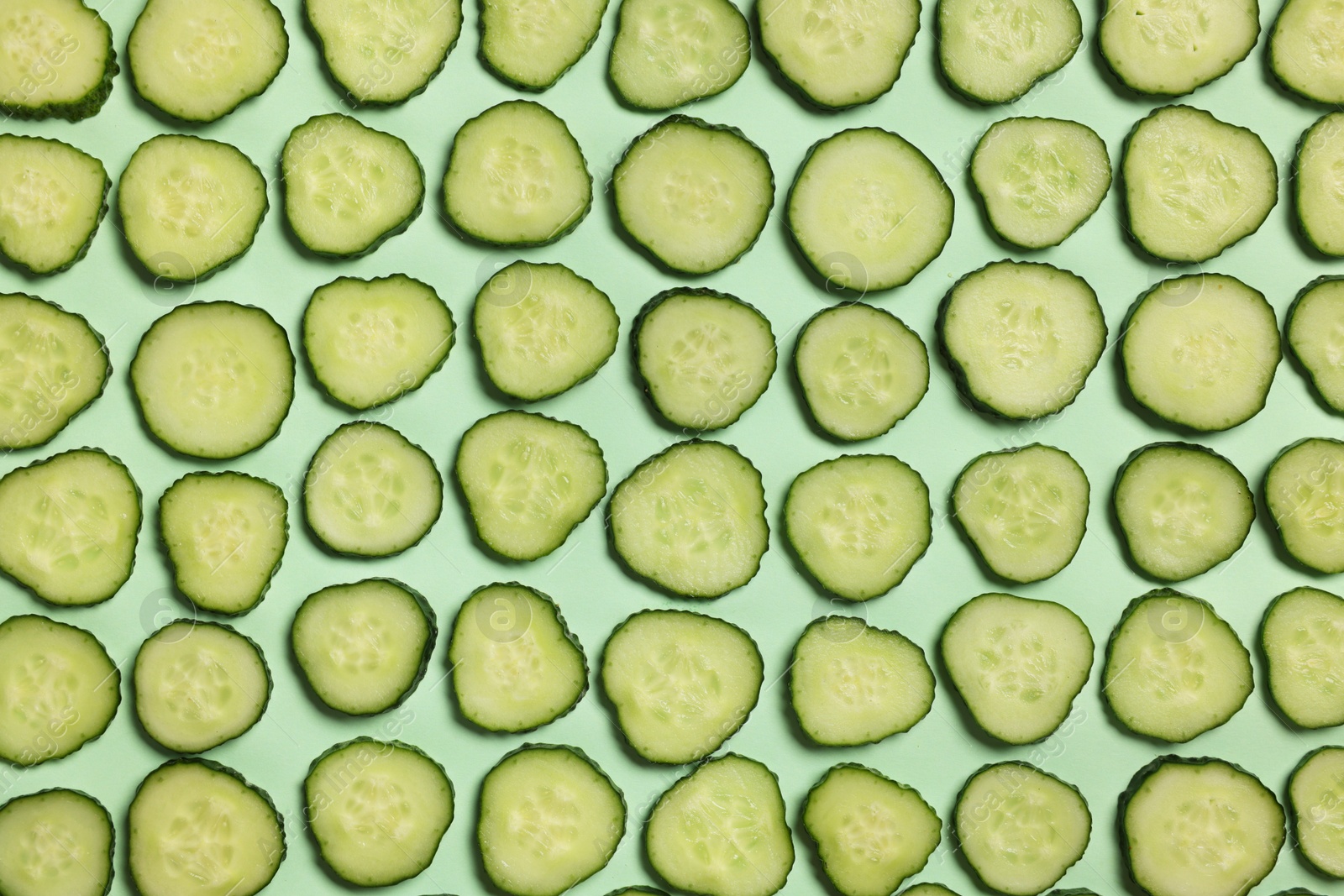 Photo of Slices of fresh cucumbers on turquoise background, flat lay