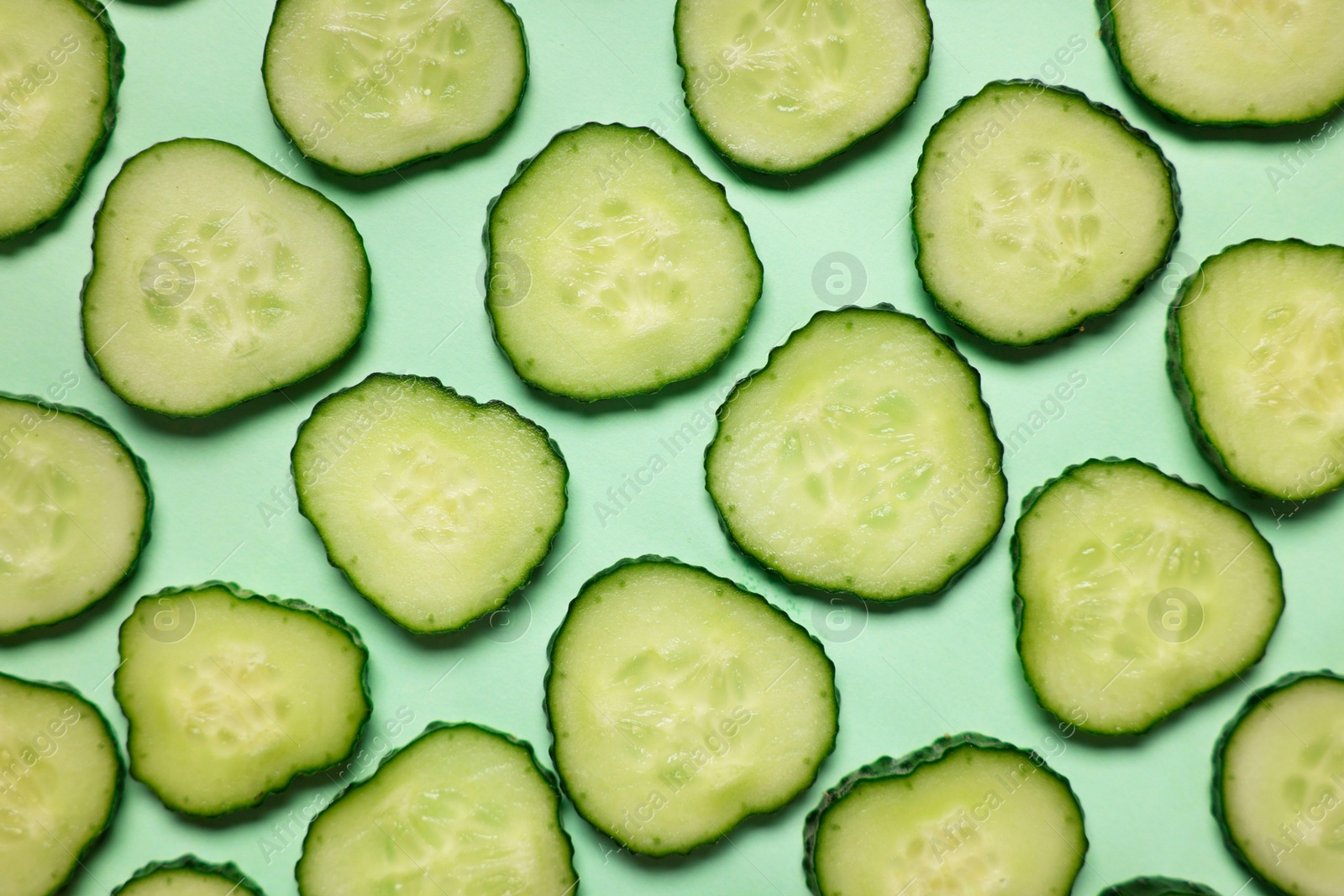 Photo of Slices of fresh cucumbers on turquoise background, flat lay