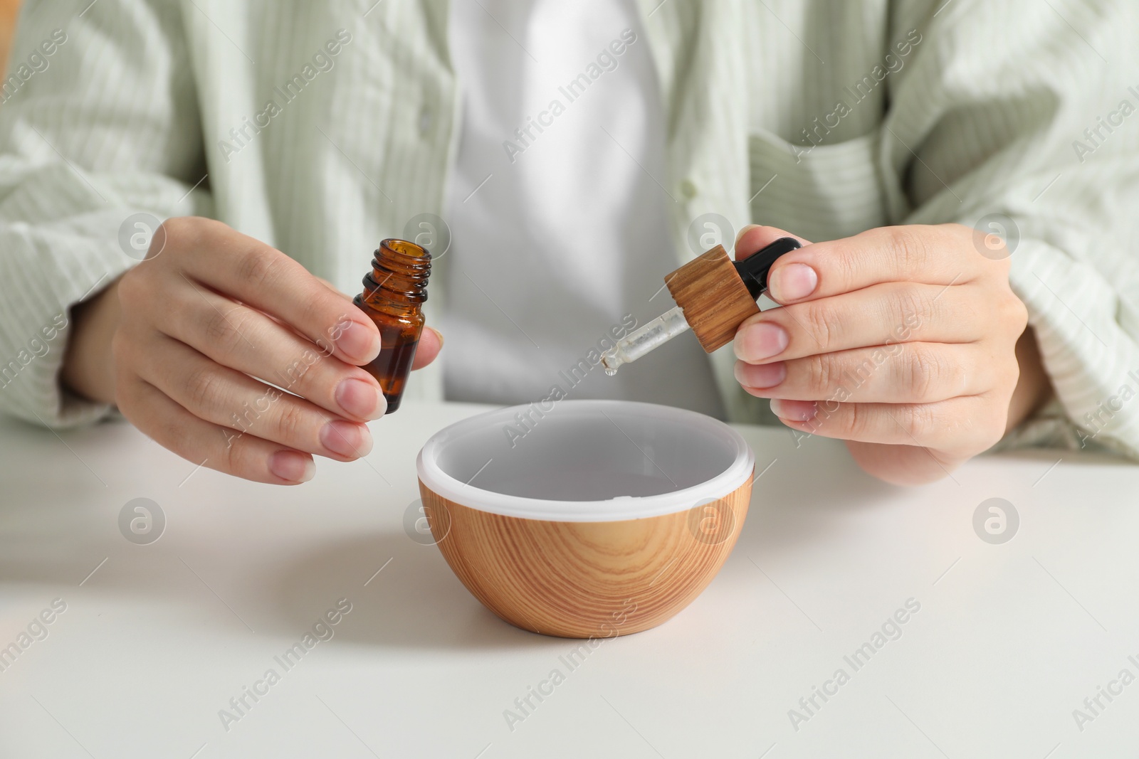 Photo of Woman adding essential oil to aroma diffuser at home, closeup