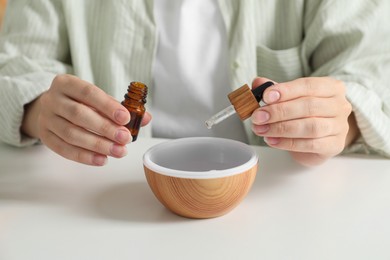 Photo of Woman adding essential oil to aroma diffuser at home, closeup