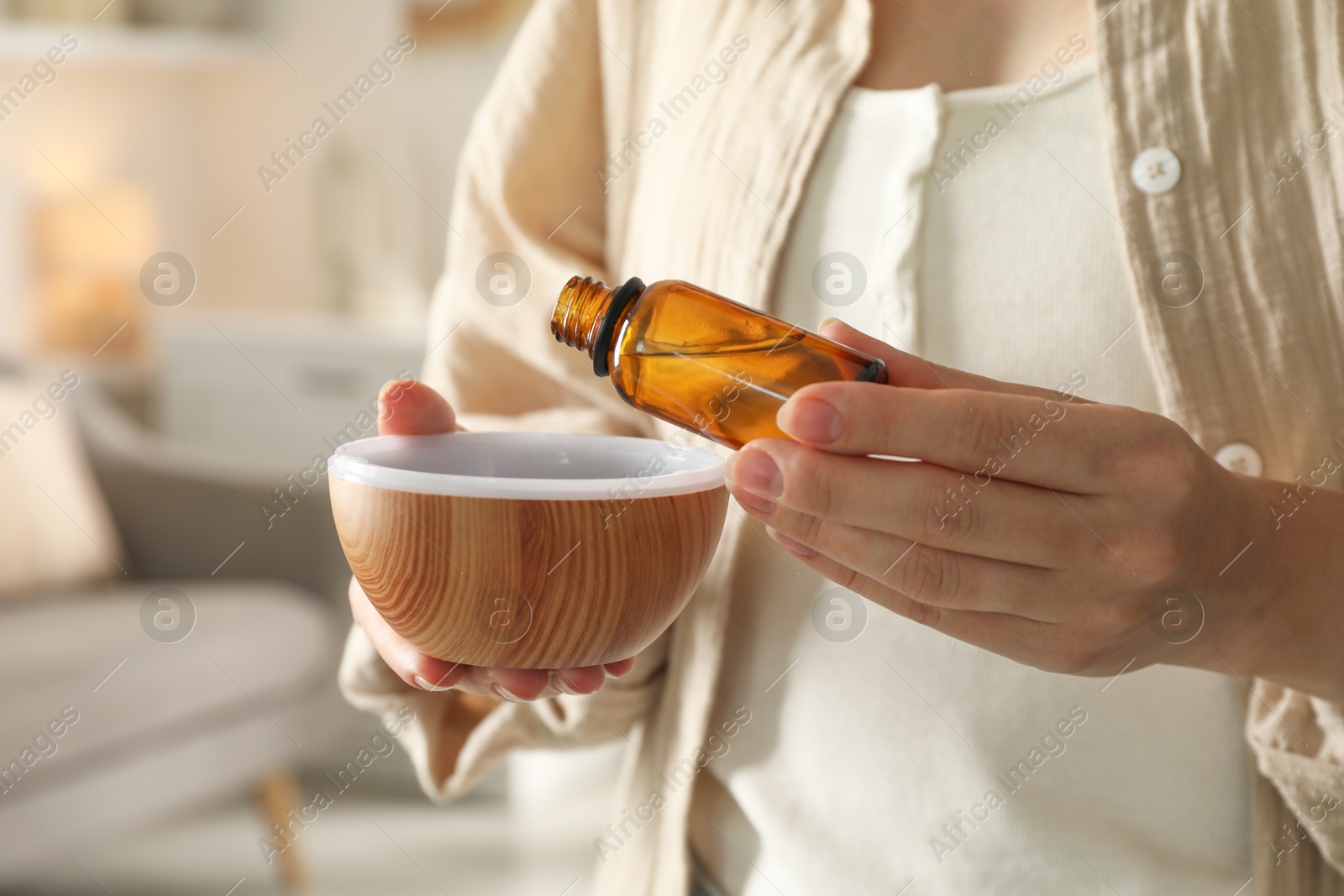 Photo of Woman adding essential oil to aroma diffuser at home, closeup