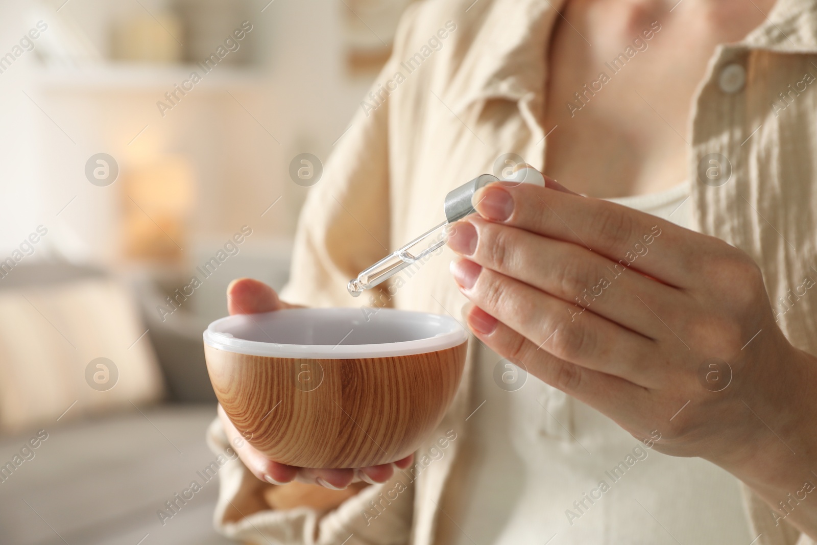 Photo of Woman adding essential oil to aroma diffuser at home, closeup