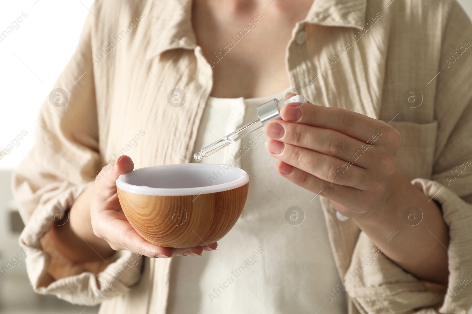 Photo of Woman adding essential oil to aroma diffuser at home, closeup