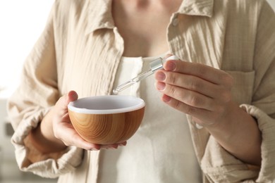 Woman adding essential oil to aroma diffuser at home, closeup