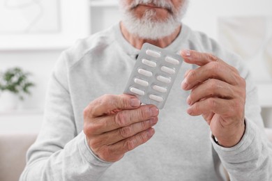 Senior man holding blister with pills at home, closeup