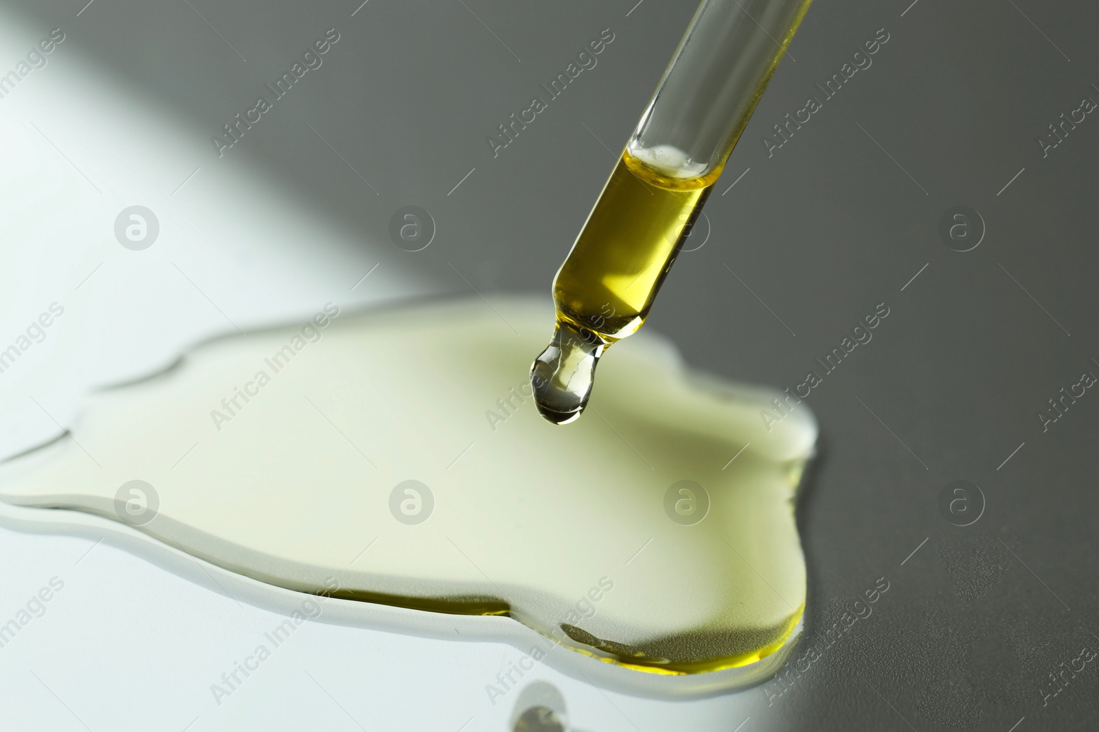 Photo of Dripping essential oil from pipette on grey background, closeup