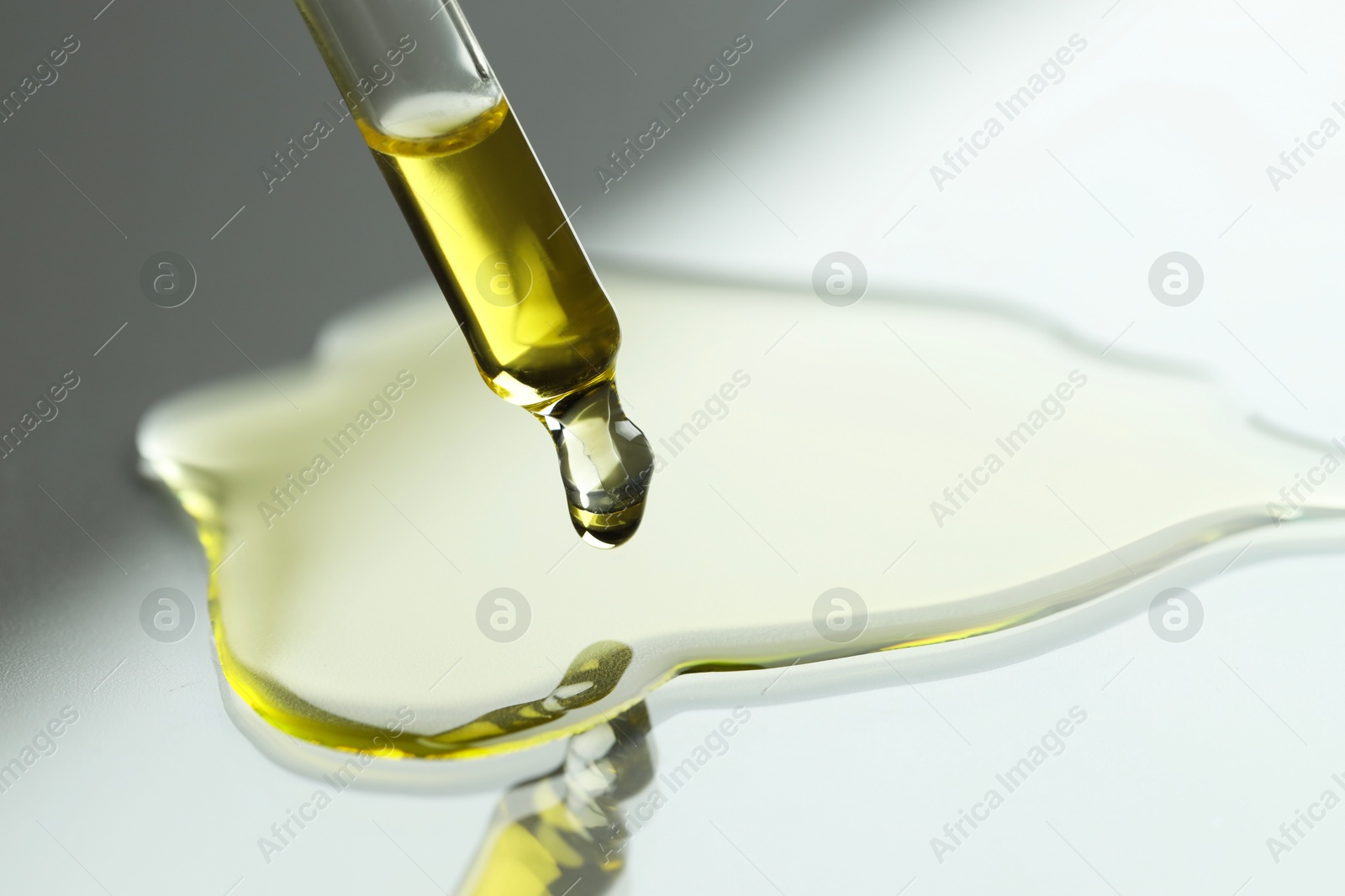 Photo of Dripping essential oil from pipette on grey background, closeup