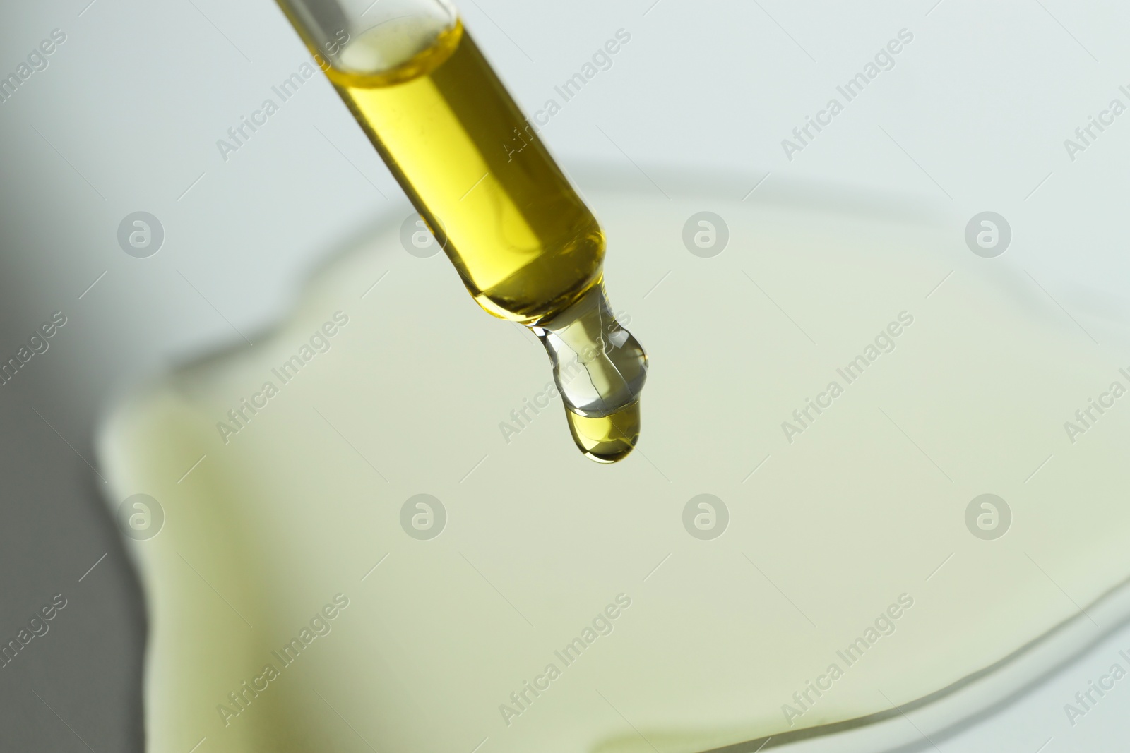 Photo of Dripping essential oil from pipette on grey background, closeup