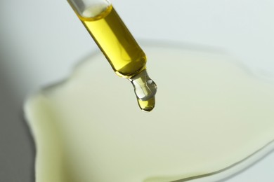 Photo of Dripping essential oil from pipette on grey background, closeup