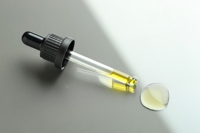 Dripping essential oil from pipette on light grey background