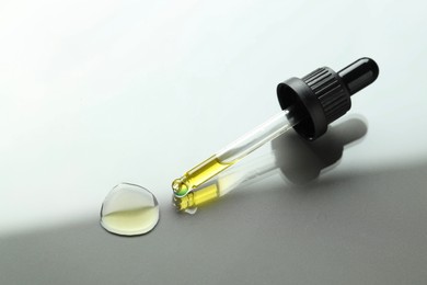 Photo of Dripping essential oil from pipette on light grey background