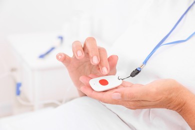 Senior woman with emergency call button on bed in hospital, closeup