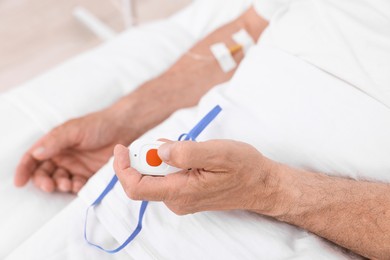 Senior man pressing emergency call button on bed in hospital, closeup