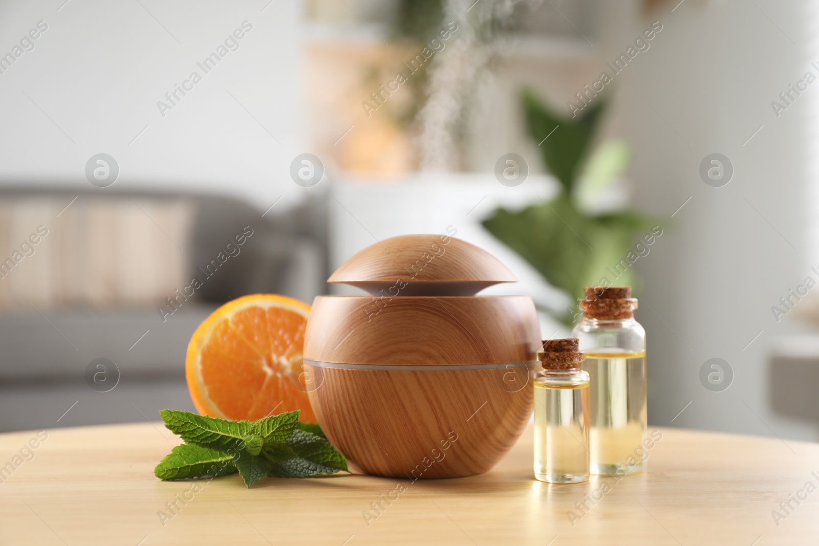 Photo of Essential oil diffuser, cosmetic products, mint and orange on wooden table at home