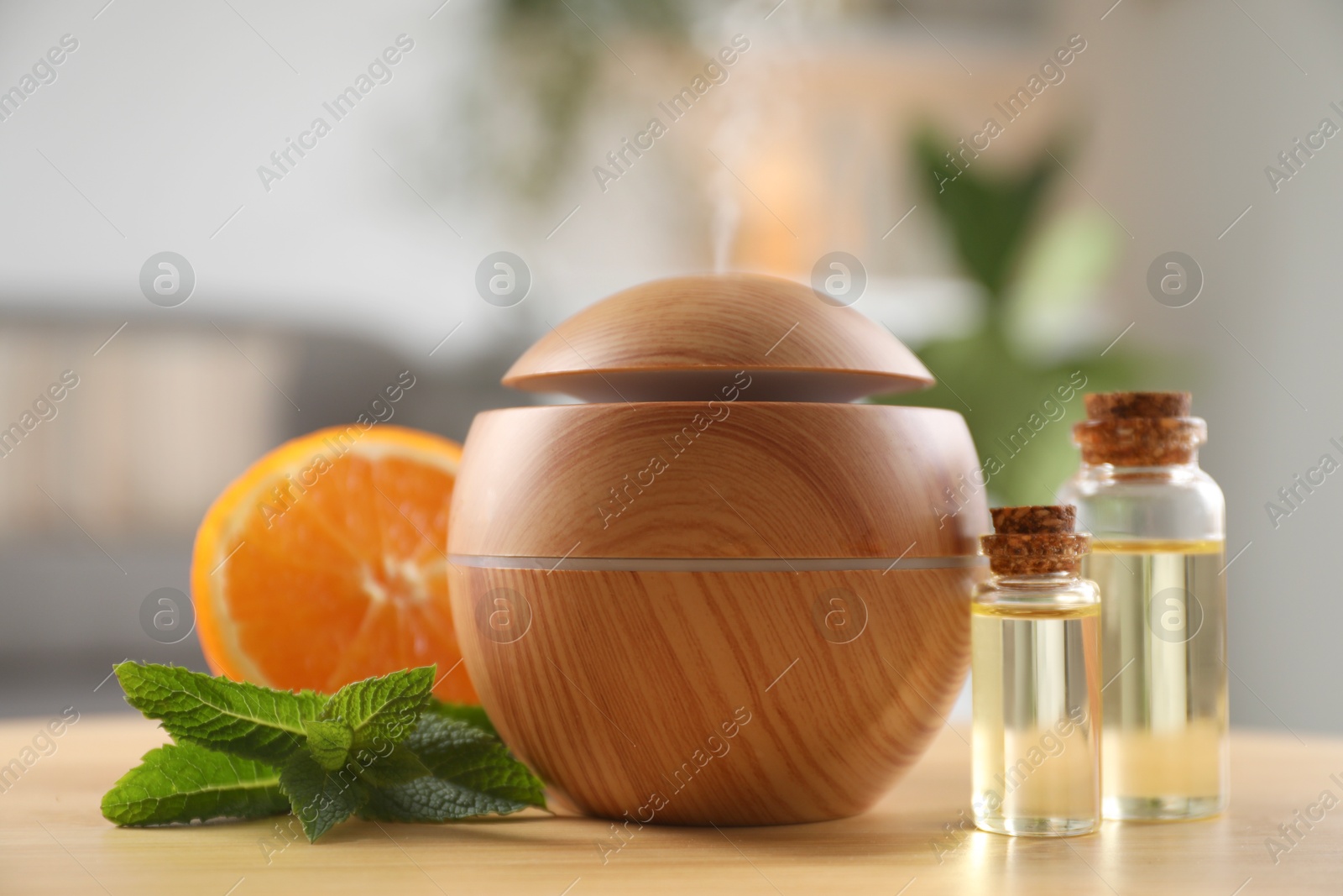 Photo of Essential oil diffuser, cosmetic products, mint and orange on wooden table at home, closeup