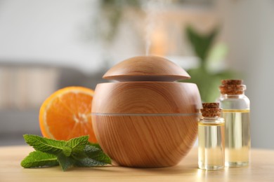 Photo of Essential oil diffuser, cosmetic products, mint and orange on wooden table at home, closeup