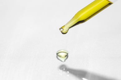 Photo of Cosmetic oil dripping from pipette on light grey background, closeup