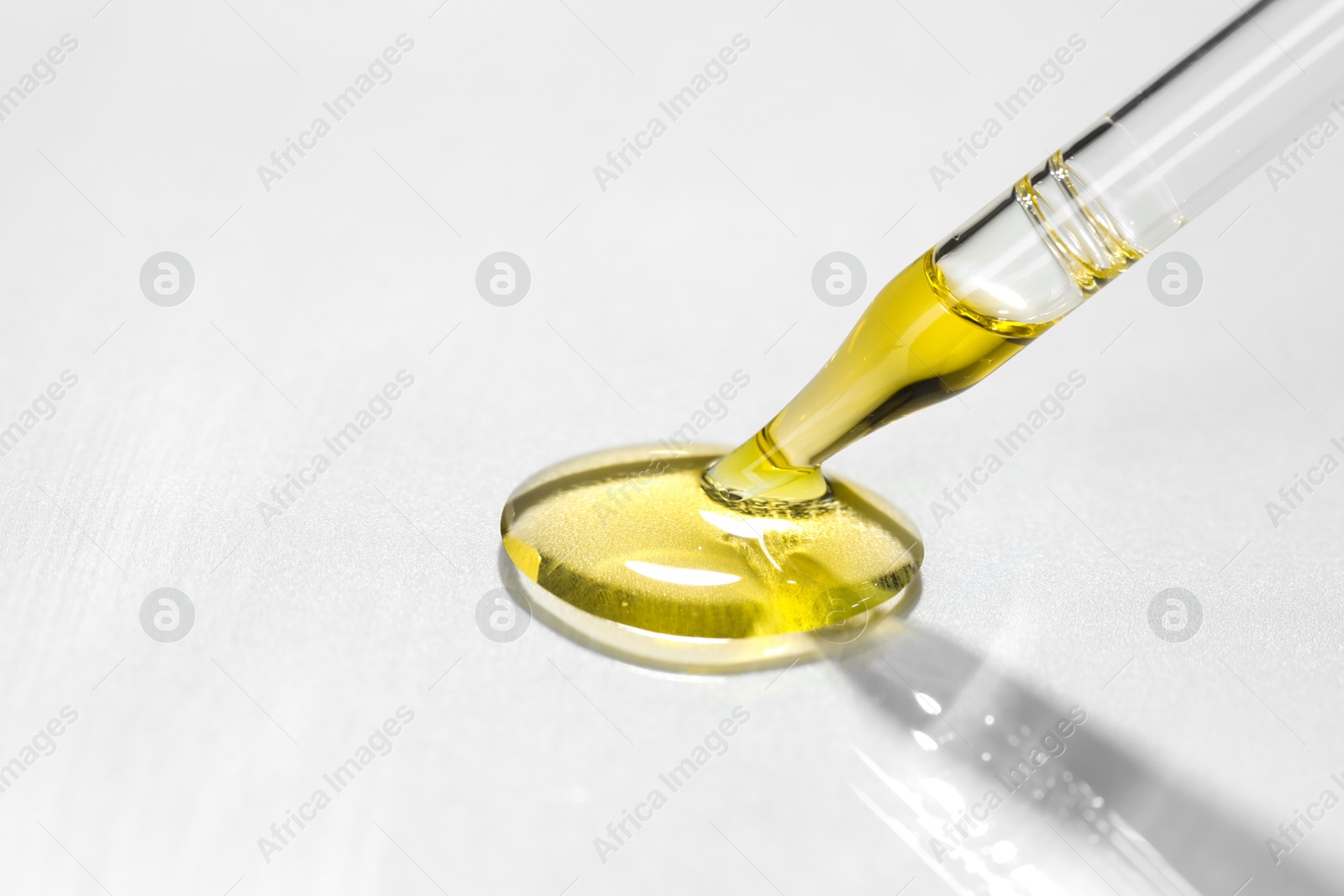 Photo of Cosmetic oil dripping from pipette on light grey background, closeup