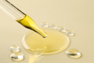 Photo of Cosmetic oil dripping from pipette on dark beige background, closeup. Space for text