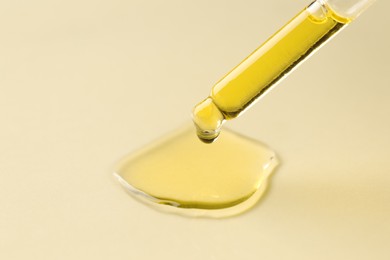 Photo of Cosmetic oil dripping from pipette on dark beige background, closeup. Space for text