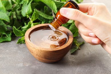 Photo of Woman dripping essential oil into bowl with water at grey table, closeup