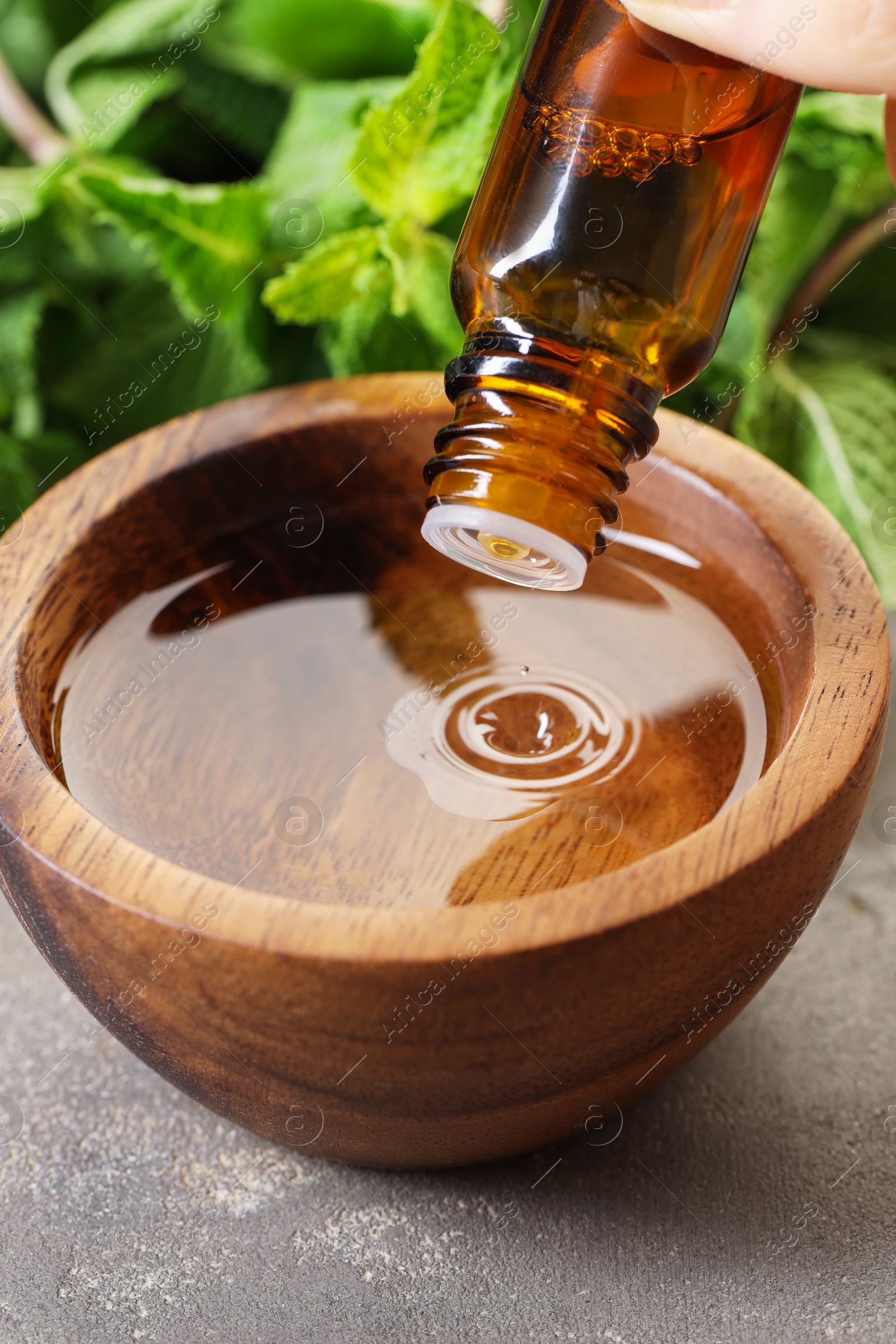 Photo of Woman dripping essential oil into bowl with water at grey table, closeup