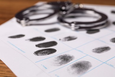 Paper sheet with human fingerprints and handcuffs on table, closeup. Criminal conviction