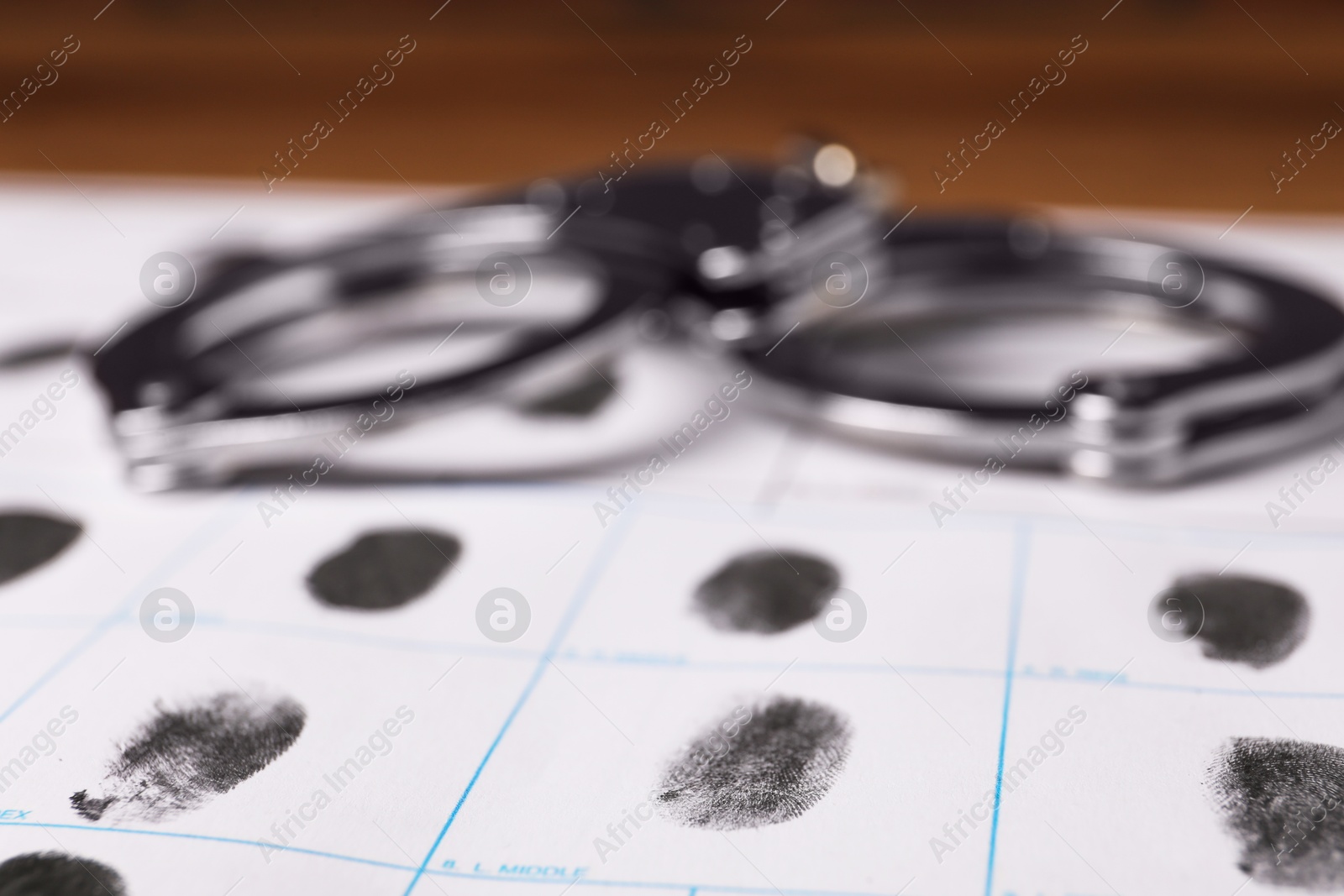 Photo of Paper sheet with human fingerprints and handcuffs on table, closeup. Criminal conviction