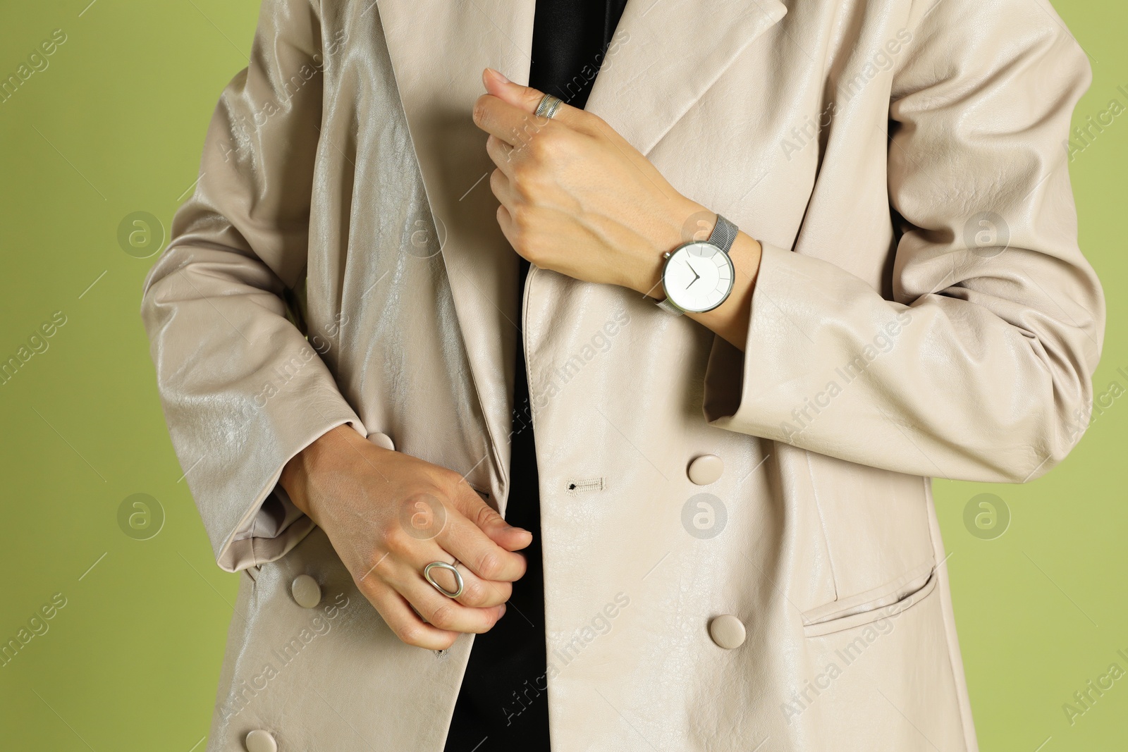 Photo of Beautiful woman in stylish beige jacket and watch on olive background, closeup