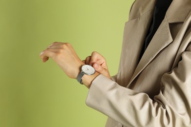 Photo of Beautiful woman in stylish beige jacket and watch on olive background, closeup