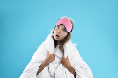 Photo of Overslept girl with sleep mask wrapped in blanket on light blue background