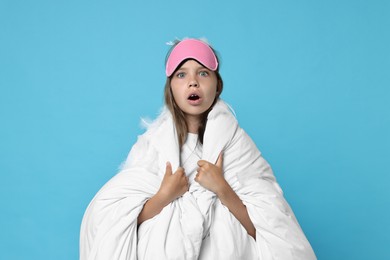 Photo of Overslept girl with sleep mask wrapped in blanket on light blue background