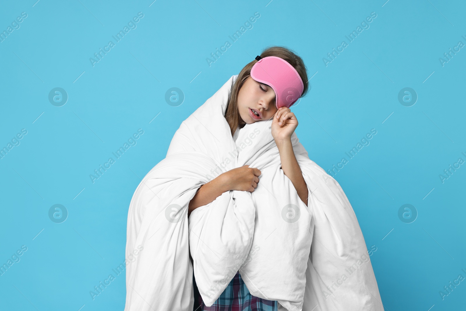 Photo of Overslept girl with sleep mask wrapped in blanket on light blue background