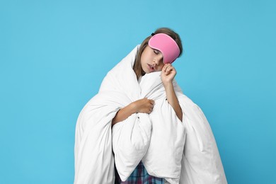 Photo of Overslept girl with sleep mask wrapped in blanket on light blue background