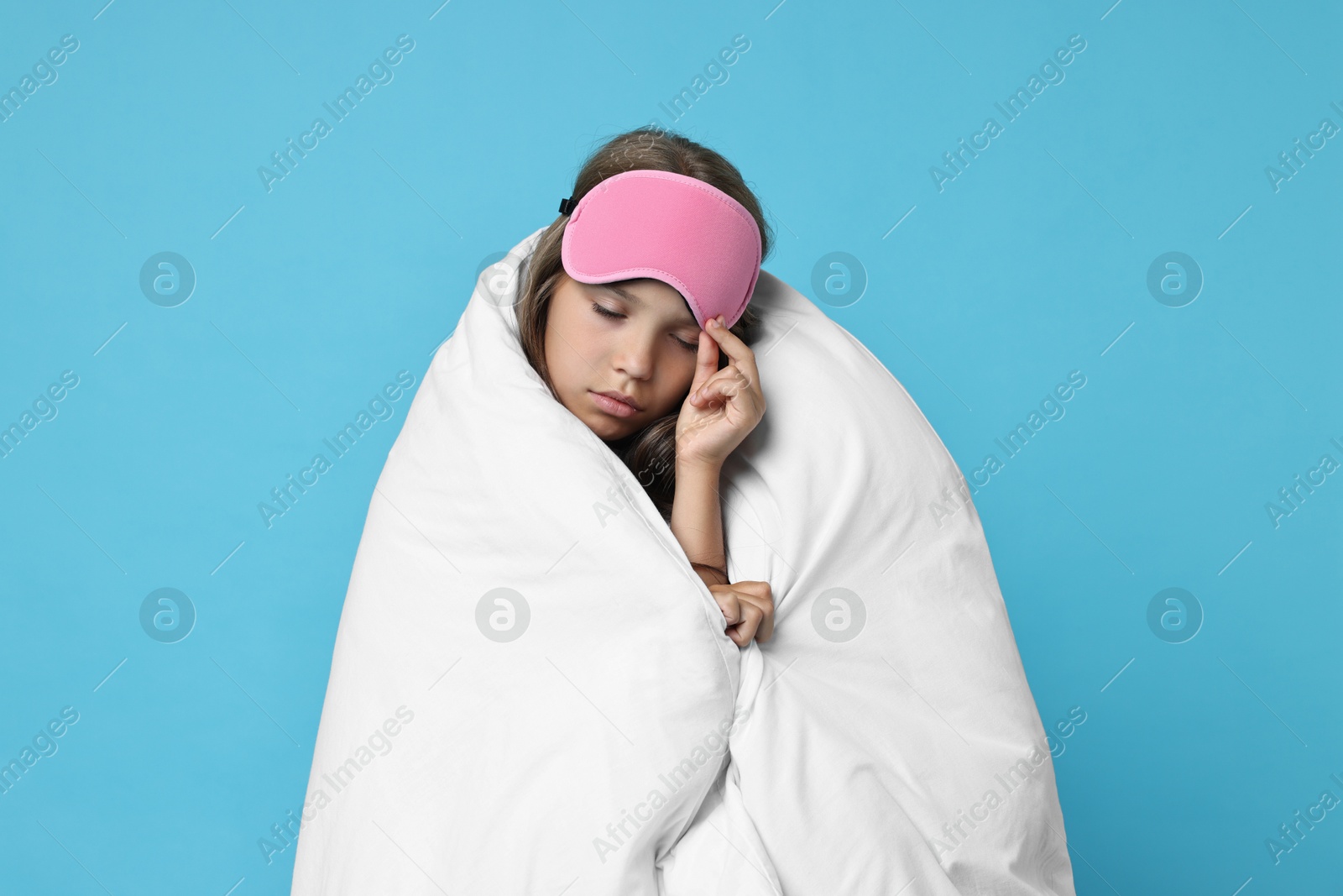 Photo of Overslept girl with sleep mask wrapped in blanket on light blue background