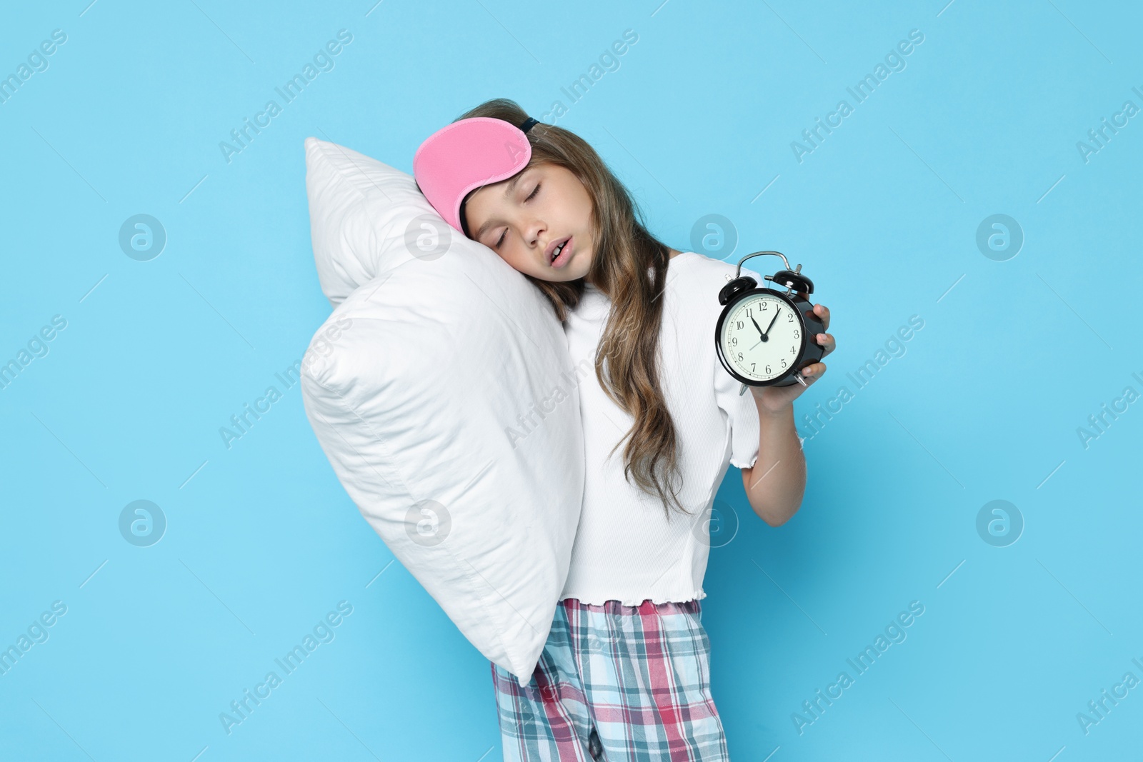 Photo of Overslept girl with sleep mask, pillow and alarm clock on light blue background