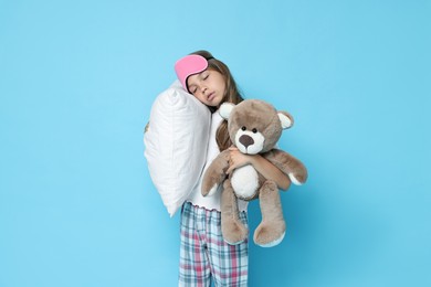 Overslept girl with sleep mask, pillow and teddy bear on light blue background