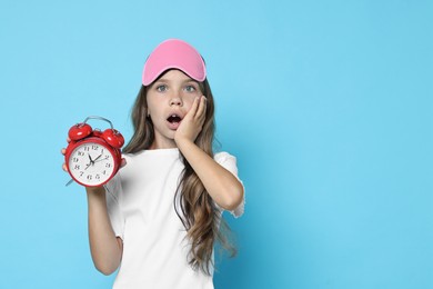 Overslept girl with sleep mask and alarm clock on light blue background, space for text