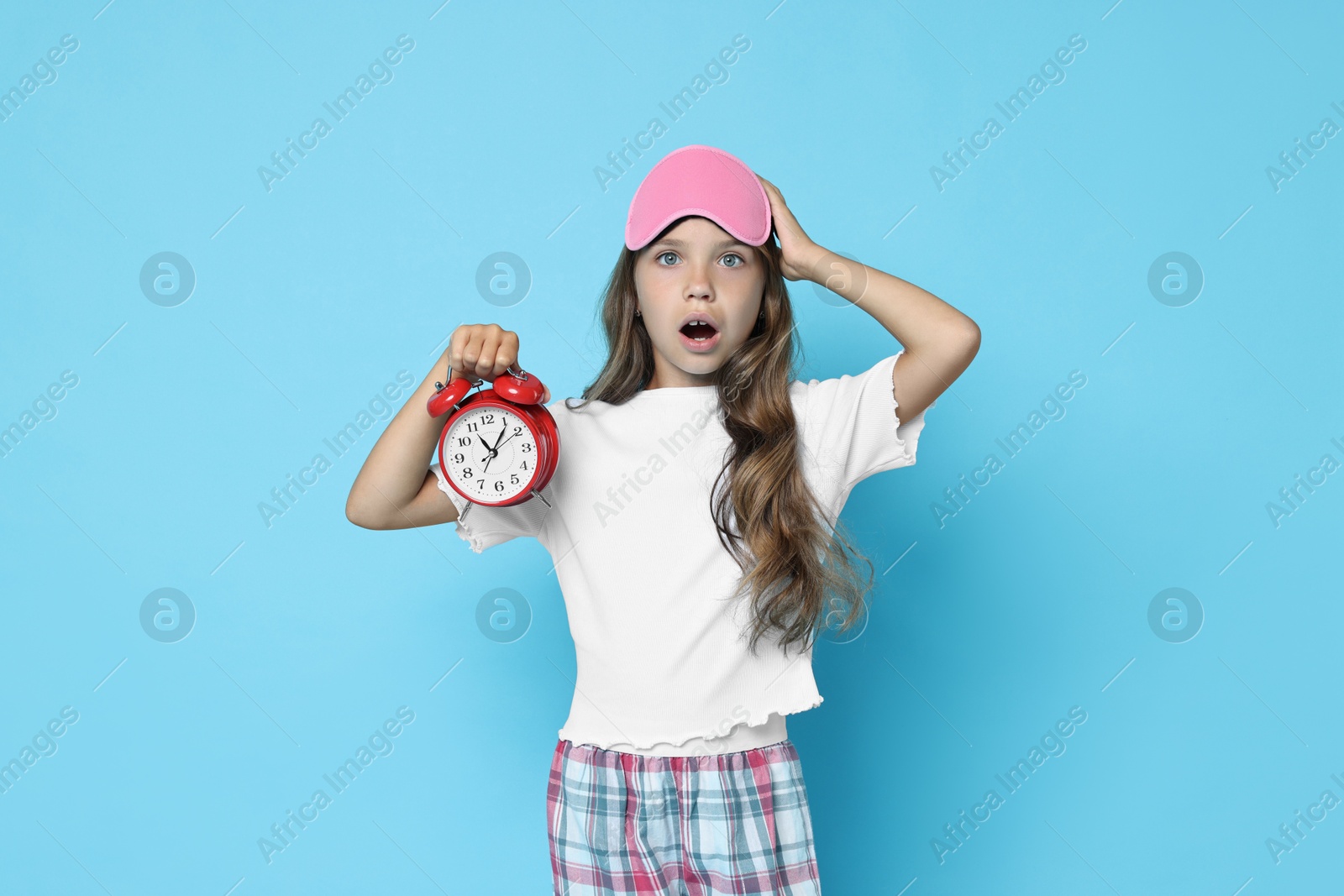 Photo of Overslept girl with sleep mask and alarm clock on light blue background